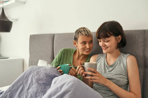 Jóvenes lesbianas descansando y tomando té en la cama —  Fotos de Stock