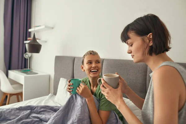 Young lesbian couple drinking tea on bed at home — Fotografia de Stock