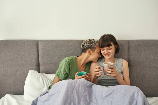 Young lesbian couple rest and drink tea on bed — Fotografia de Stock