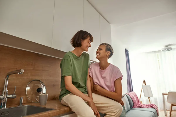 Lesbianas pareja mira el uno al otro en casa cocina — Foto de Stock