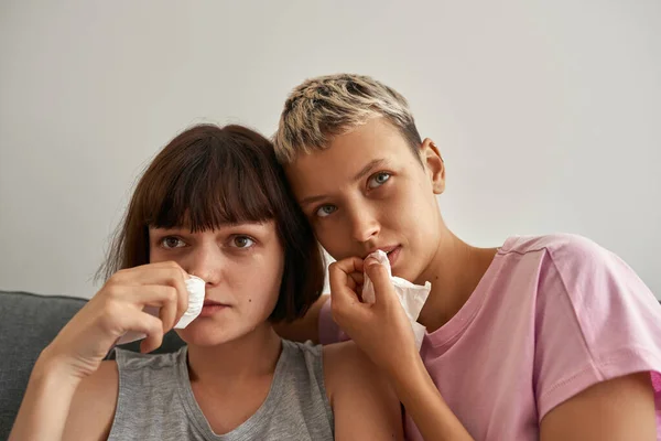 Sad girls watching TV and crying on sofa at home — стоковое фото