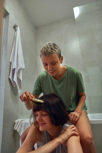 Girl combing hair of her girlfriend at bathroom — Zdjęcie stockowe