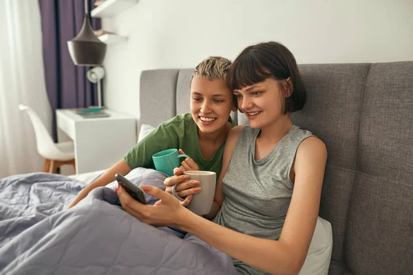 Lesbians watch on smartphones and drink tea — Fotografia de Stock
