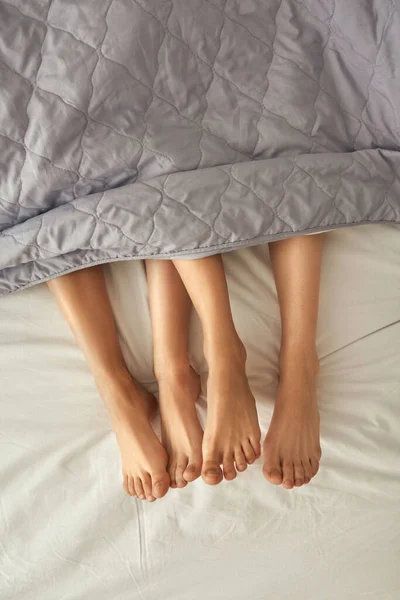 Обрізані ноги дівчат під ковдрою на ліжку — стокове фото
