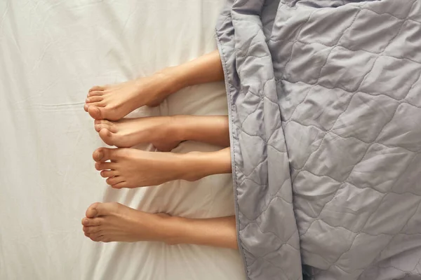 Gedeeltelijk van benen van meisjes onder deken op bed — Stockfoto