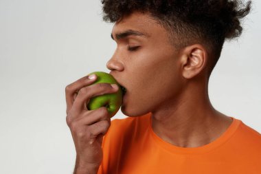 Kapalı gözlü siyah adam yeşil organik elma yiyor.