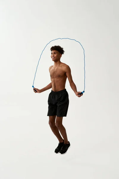 Black smiling sportsman jumping on skipping rope