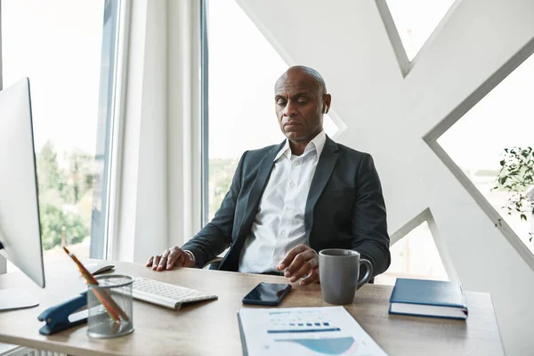 Black businessman sitting at desk and thinking — Stockfoto