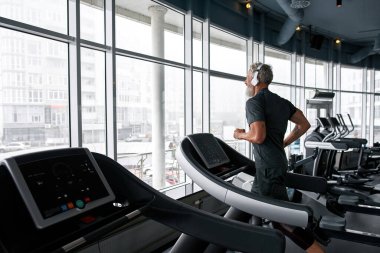 Strong aged man running on treadmil, back view