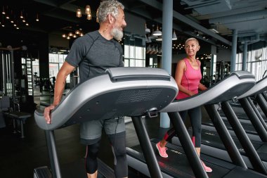 Handsome aged man flirting with lovely middle-aged woman in gym