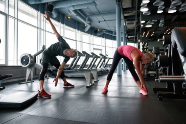 Stretching after workout in gym. Senior couple bending