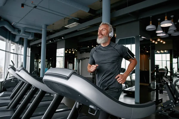 Active senior man jogging on treadmill in sports center — Foto Stock
