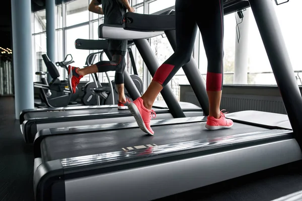 Lower legs part of fitness woman and man running on running machine — Fotografia de Stock