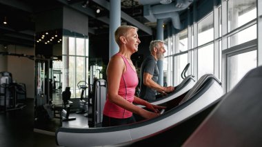 Active senior couple exercising on treadmills in gym