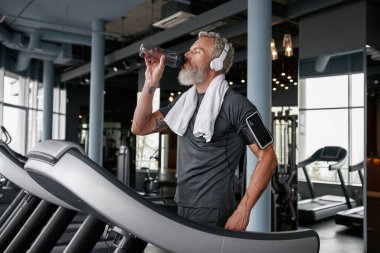 Senior man drinking water after running on treadmill