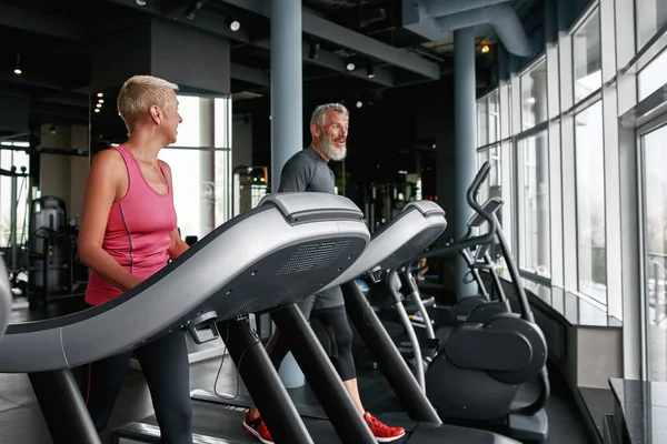 Elderly woman and man walking on treadmill in gym — Zdjęcie stockowe
