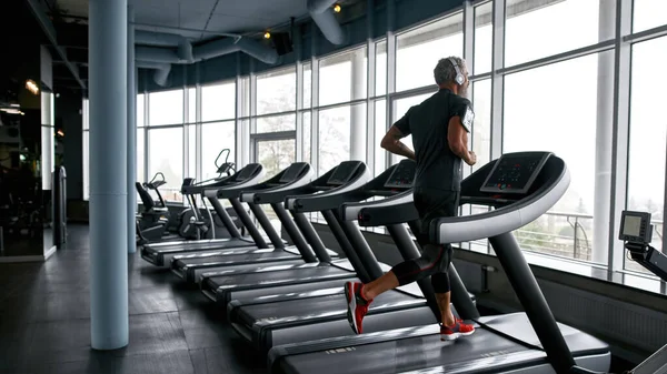 Man listening to music via headphones and running on treadmill — Stock Photo, Image