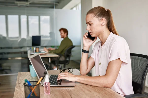 Side of girl talk on smartphone and type on laptop — Stok fotoğraf