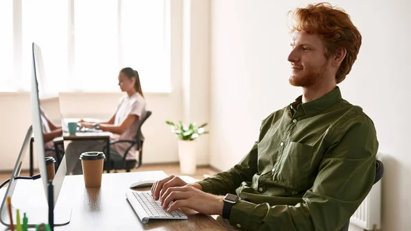 Smiling caucasian man typing on laptop at work — Foto de Stock