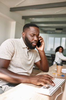 Man talking on smartphone and typing on computer