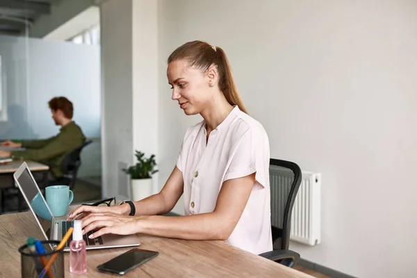Smiling girl typing on laptop while working — Stok fotoğraf