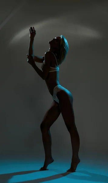 Zijaanzicht atletische jonge vrouw in ondergoed poseren in blauw licht — Stockfoto