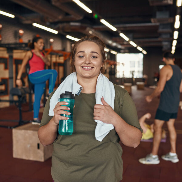 Женщина смотрит в камеру с людьми, упражняющимися в спортзале