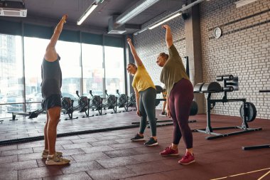 Beyaz kızlar spor salonunda antrenörle esniyorlar.