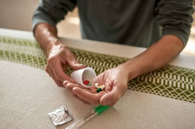 Yaşlı hasta adam plastik bardaktaki hapları avuç içine koydu.