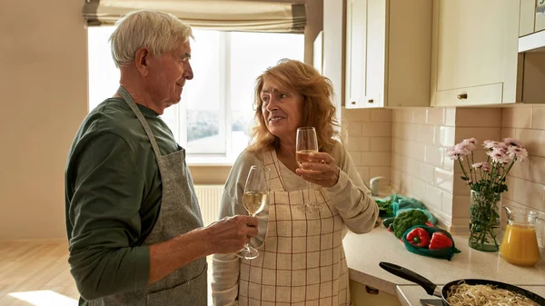 Casal de idosos bebendo vinho enquanto cozinha em casa — Fotografia de Stock