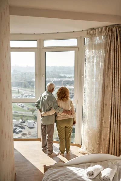高齢者のカップル抱擁と窓から街を見て — ストック写真