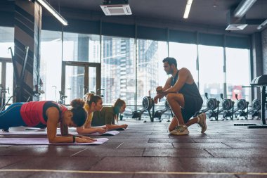 Eğitmen kalas egzersizi yapan kızlara bakıyor.