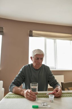 Gri saçlı hasta adam haplarla paket arıyor.