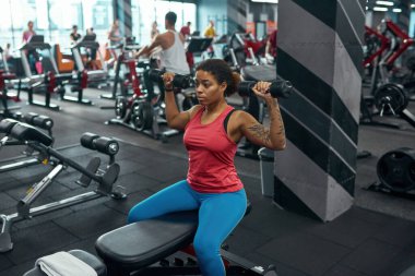 Kadın omuzlarında dambıllarla egzersiz yapıyor.