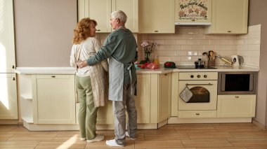 Adam mutfakta yemek pişirirken karısına sarılıyor.