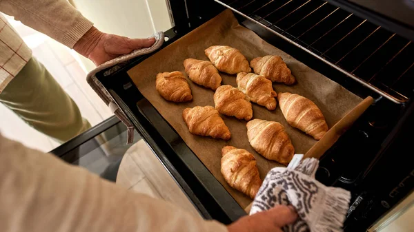 Kıdemli adam kruvasanla tepsiyi fırından alıyor.
