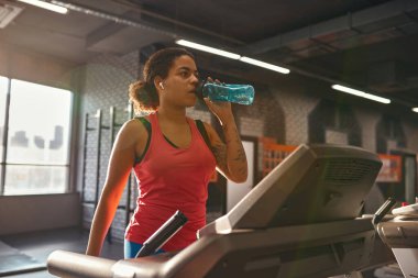 Koşu bandında koşarken su içen kız