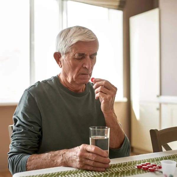 Homem doente sênior com copo de água tomando pílula — Fotografia de Stock