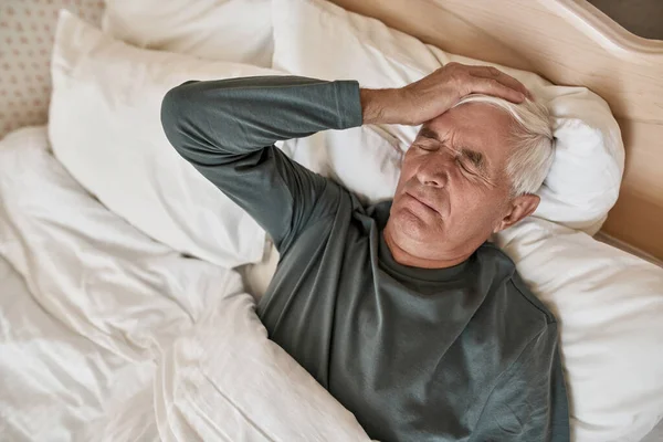 Γκρίζα μαλλιά άνθρωπος με πονοκέφαλο ξαπλωμένος στο κρεβάτι στο σπίτι — Φωτογραφία Αρχείου