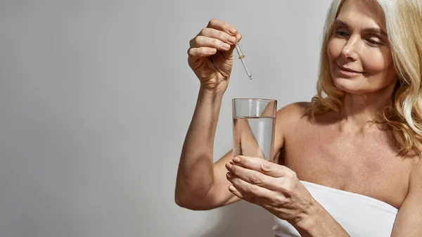 Mulher pingando de pipeta em vidro com água — Fotografia de Stock