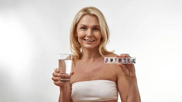 Mujer mostrando vidrio con agua y conjunto con píldoras — Foto de Stock