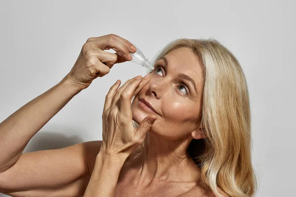 Mujer europea madura goteando gotas en los ojos — Foto de Stock