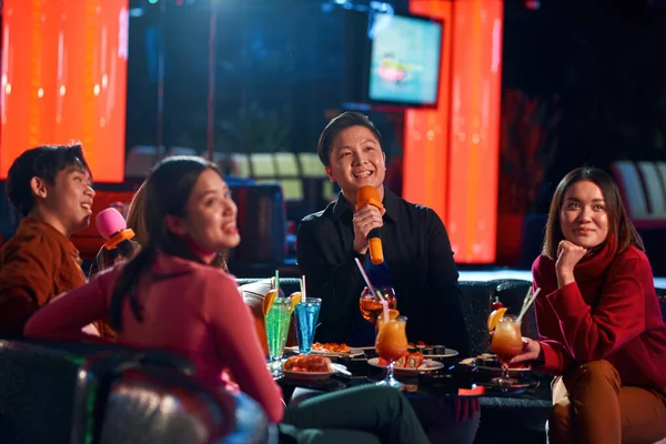Unga glada asiatiska människor som har roligt medan de sjunger karaoke på kvällsfest på bar. — Stockfoto