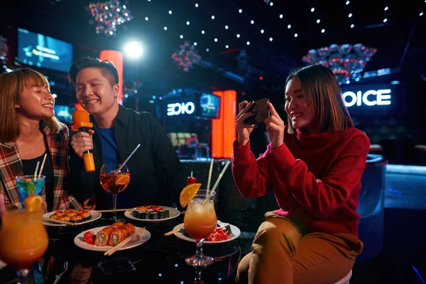 Chica tomando fotos a sus amigos en la fiesta de karaoke en el club — Foto de Stock