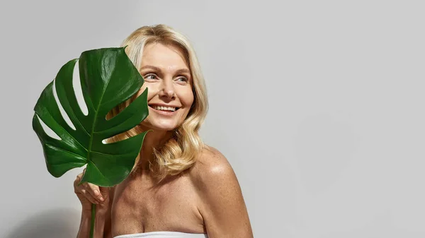 Sonriente mujer de mediana edad sosteniendo gran hoja verde — Foto de Stock