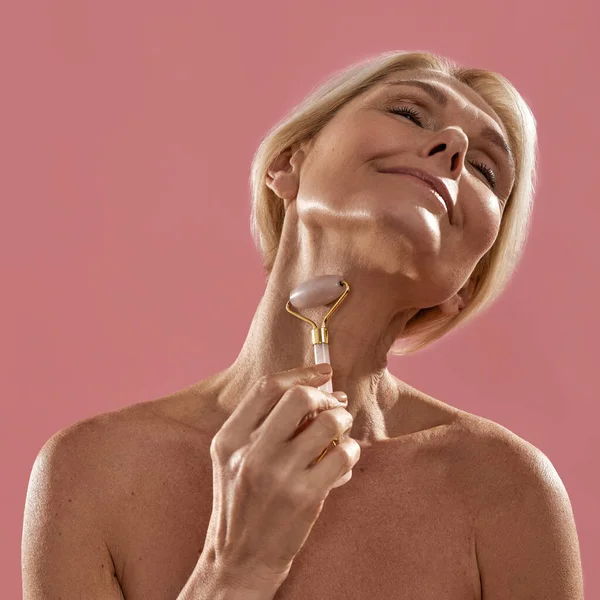 Mature woman massaging her neck with jade roller — Stock Photo, Image