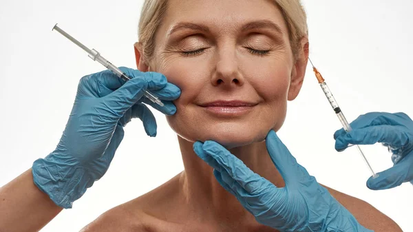 Lekarze wykonujący wstrzyknięcie na twarz kobiety w średnim wieku — Zdjęcie stockowe