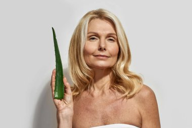Kendinden emin olgun bir kadın aloe vera yaprağı tutuyor.