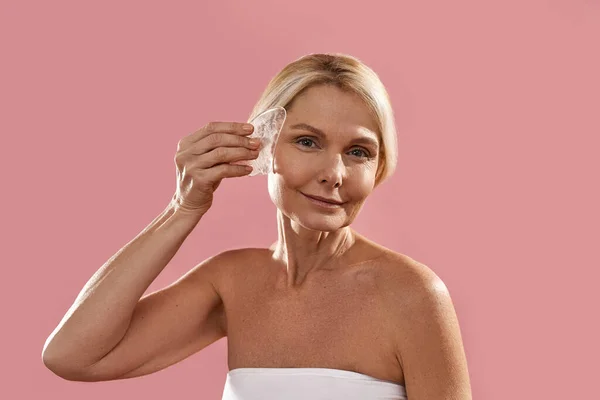 Mature caucasian woman apply ice slice on her face — Stock Photo, Image