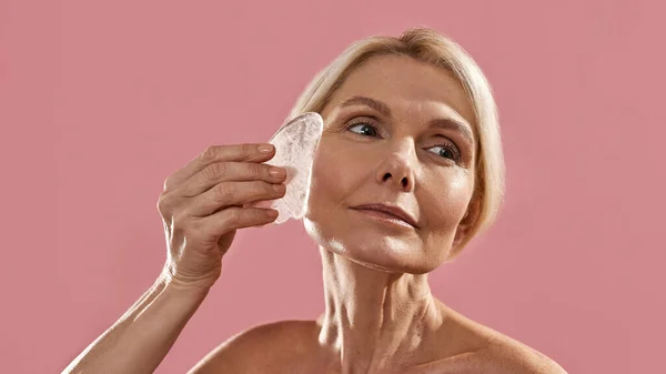 Mulher de meia idade aplicando fatia de gelo em seu rosto — Fotografia de Stock